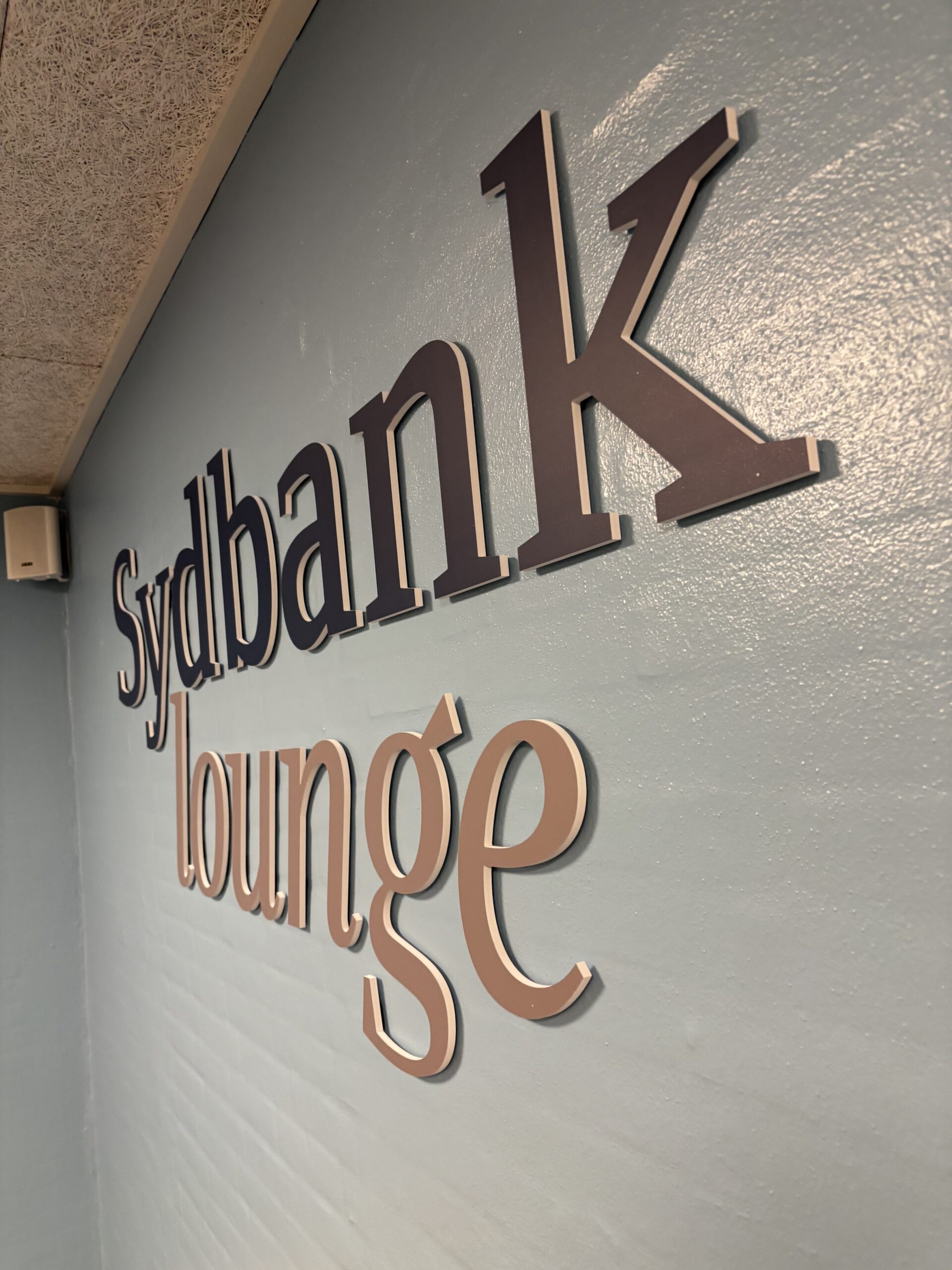 Indendørs facadelogo med 3D-bogstaver for Sydbank lounge, monteret som elegant og professionel skiltning.