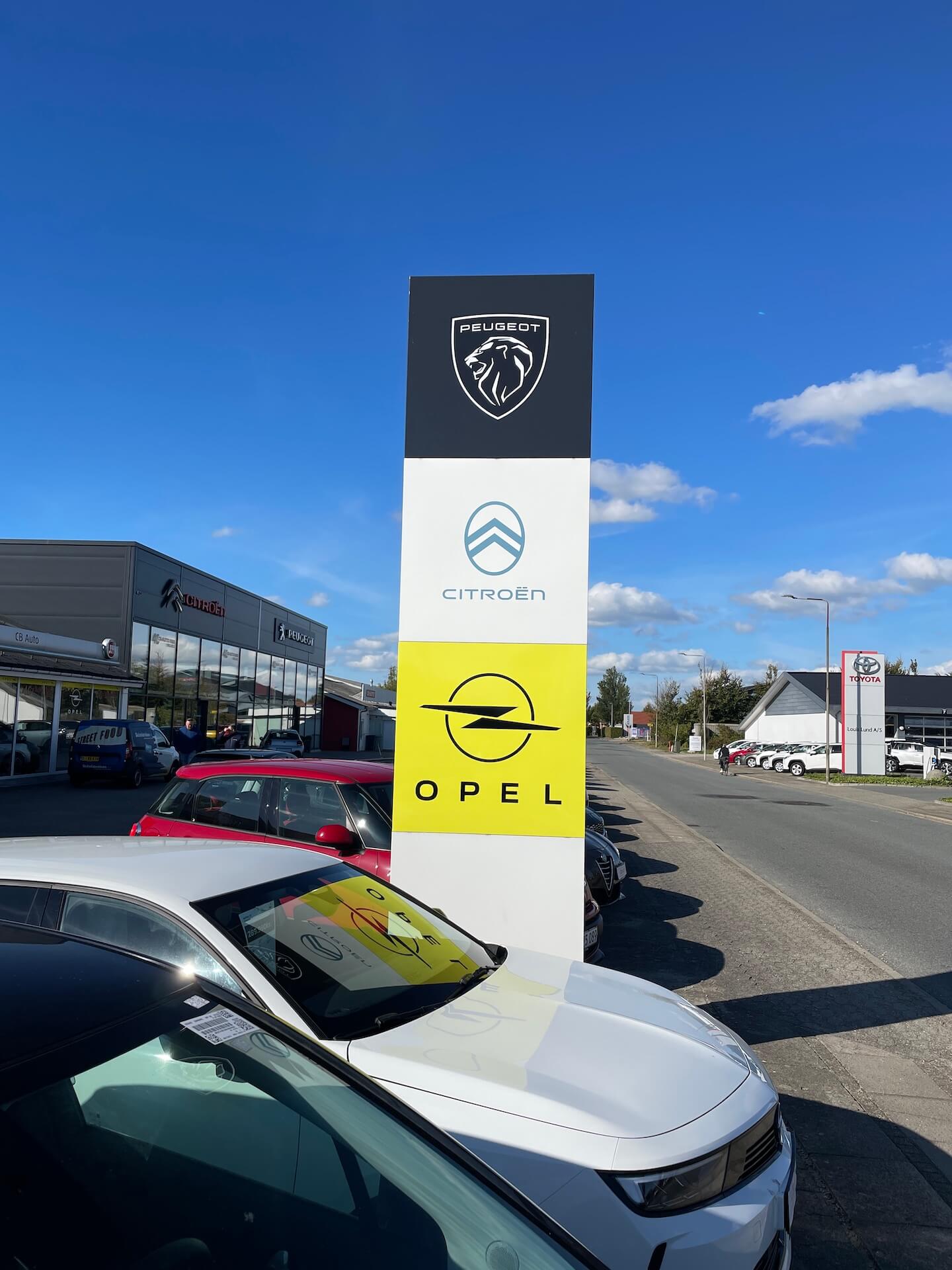 Skiltepylon i tre sektioner med bilbrands, anvendt som markant udendørs skiltning ved forhandler.