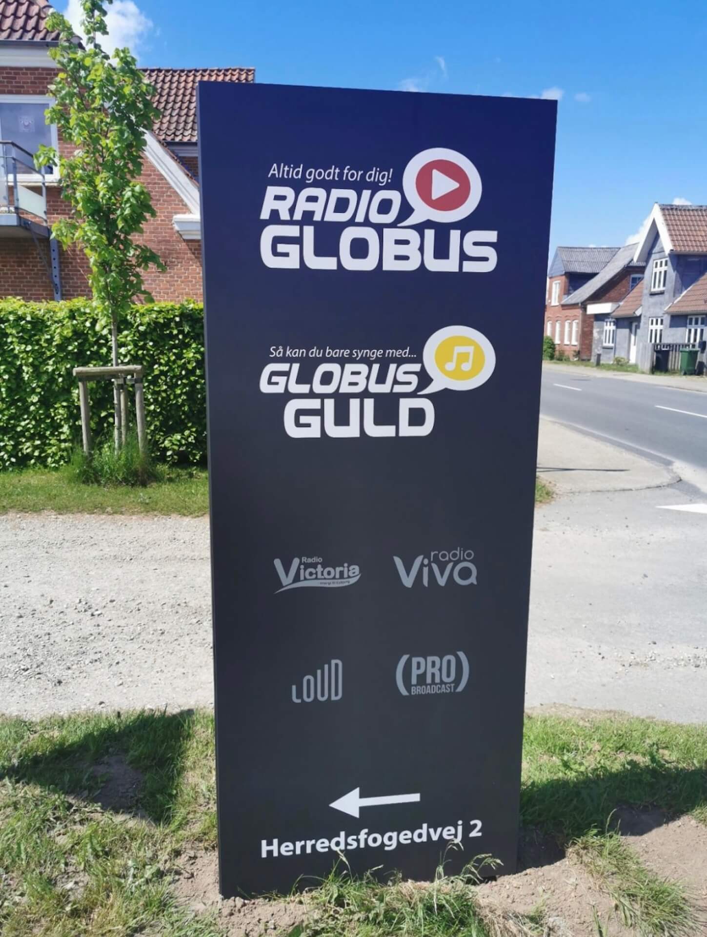 Reklamepylon med logo ved indkørsel til Radio Globus og Globus Guld, der giver synlig branding og klar orientering.
